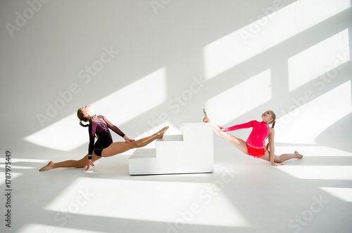 two young beautiful gymnast girls posing in white studio