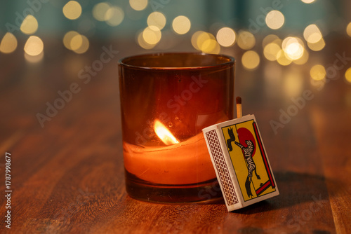 Cuadro en lienzo A lit candle in a brown glass holder glows warmly beside a matchbox on a wooden surface