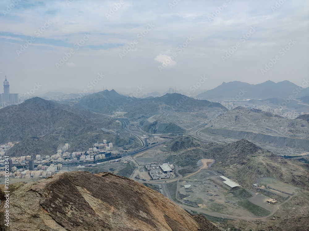 Obraz premium Soft clouds drift across hazy mountains and a sprawling valley, revealing distant towns and winding roads—an inviting, expansive scene for explorers and photographers.