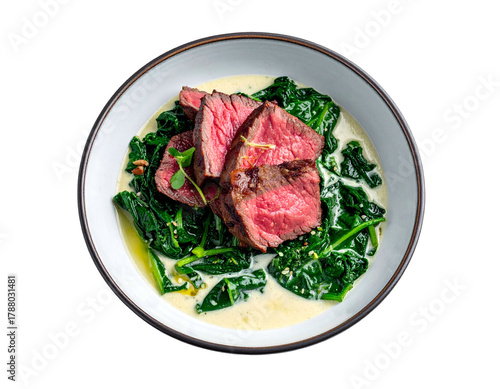 Plate of seared steak over creamed spinach in a bowl, top-down view on black