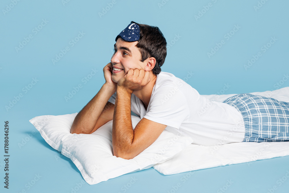 Obraz premium Side profile view calm dreamful minded young man he wears pyjamas jam sleep eye mask rest relax at home lying on bed isolated on plain pastel light blue cyan background. Good mood night nap concept.