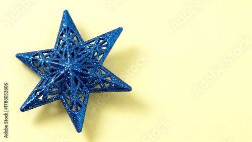 Blue glittery star ornament on pastel yellow background. Minimal holiday celebration theme.