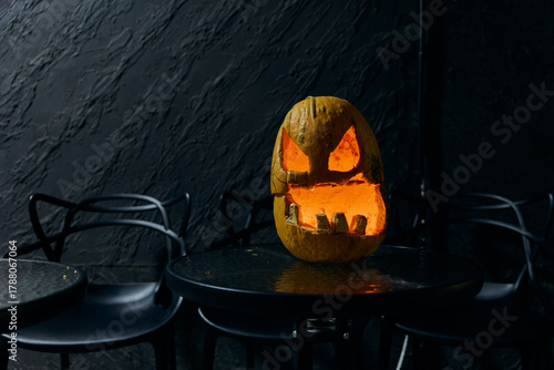 A scary Halloween pumpkin head glows from within on the table.