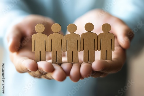 Hand Holding Miniature Figures: A person holds a row of miniature wooden figures, signifying unity, teamwork, and the importance of human connection