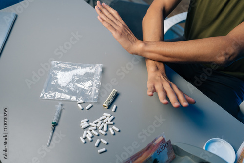Recovering drug user pushing away narcotics, surrounded by scattered medical tools and paraphernalia, representing personal battle against substance dependency. Concept of healthy lifestyle.