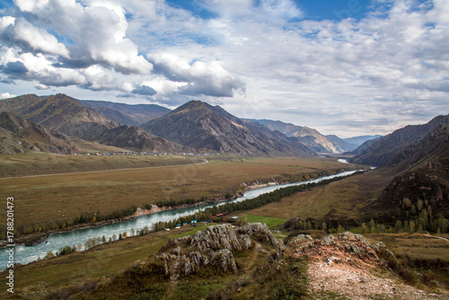 A fast-flowing cold river winding through the autumnal landscape of the Altai Republic, Russia surrounded by golden trees and rugged mountain scenery