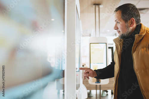 Man using self-service touchscreen kiosk in modern restaurant, interacting with digital ordering system, choosing items on interactive display, concept of technology, automation, and customer convenie