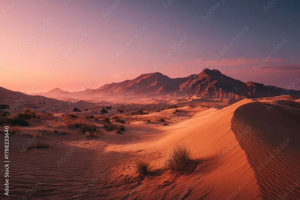 Fototapeta premium Serene desert landscape with soft dunes and gentle hues, featuring dry grass clusters, majestic mountains, and a pastel sky at dawn or dusk, inviting moments of tranquility and reflection