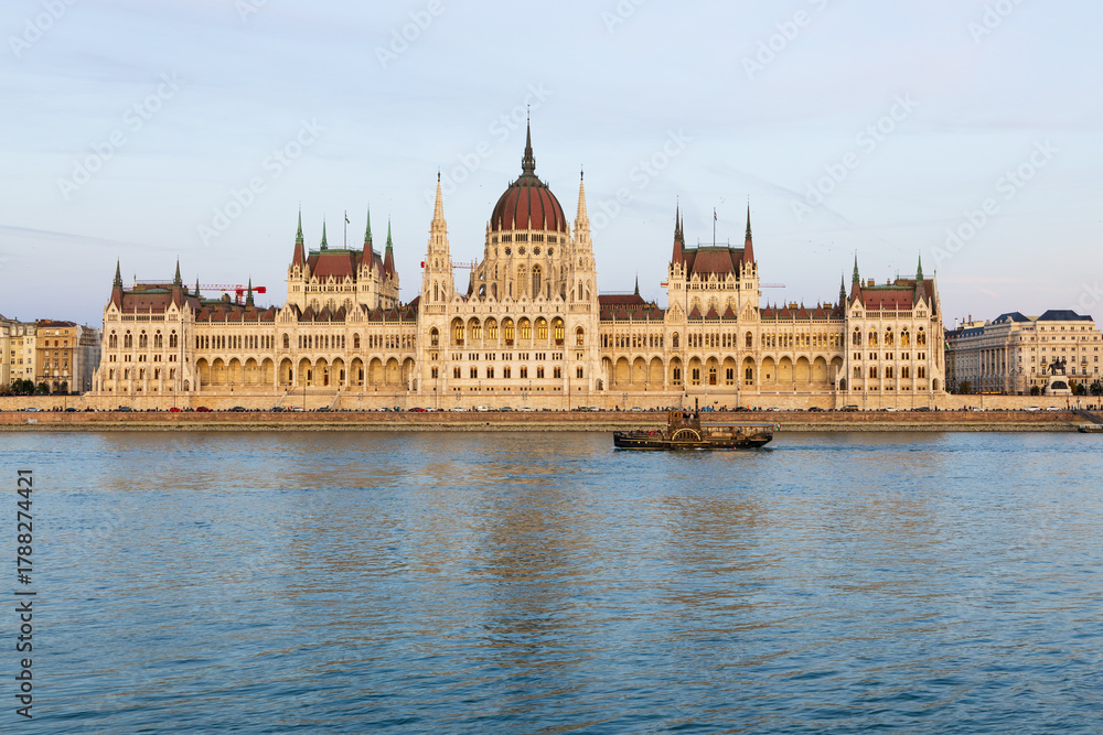 Fototapeta premium Old-fashioned paddle boat moving along the Danube river in front of the 1905 Gothic Renaissance style Parliament seen from Buda during the afternoon golden hour, Budapest, Hungary