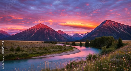 Majestic mountain peaks bathed in vibrant sunset colors over a serene river landscape