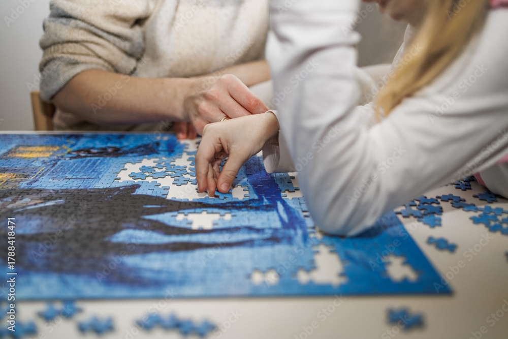 Obraz premium Mother and daughter focusing on a large jigsaw puzzle together. Symbol of family connection, concentration, and creativity at home