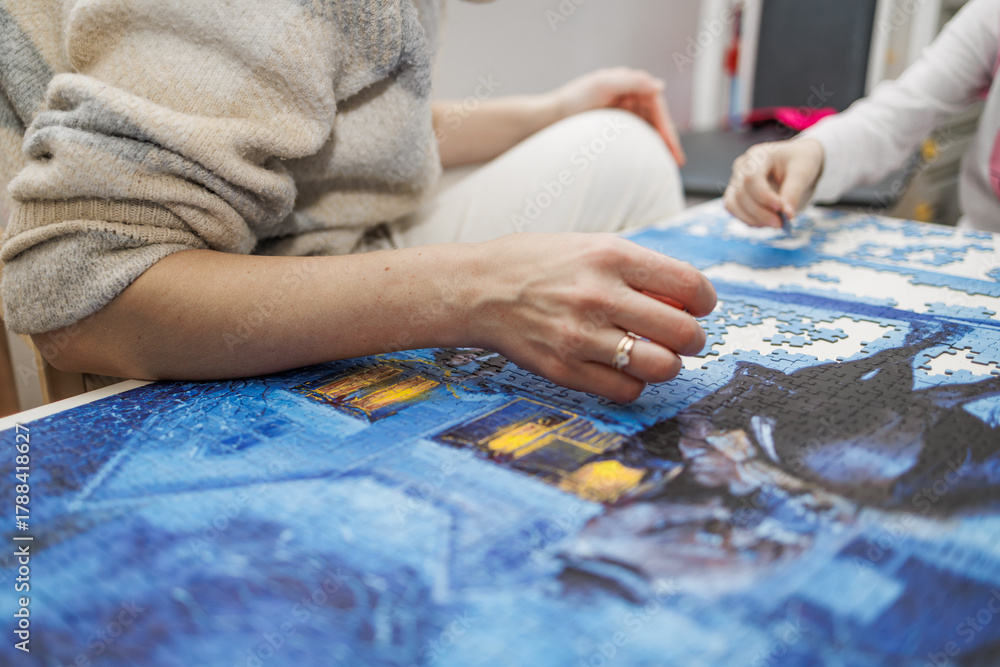 Fototapeta premium Mother and child assembling a large blue jigsaw puzzle at home. Concept of creativity, family bonding, and mindful learnin