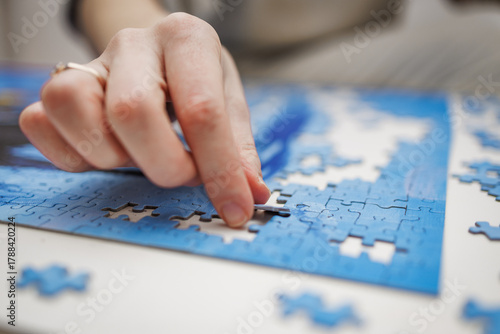 Close-up of a female hand placing a puzzle piece on a table. Creative, mindful activity that promotes focus and relaxation