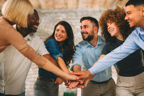 Diverse, multi-ethnic business team stacking hands in the center, showing unity, teamwork, and success in a modern office