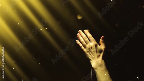 A man clasps his hands in prayer, enveloped in yellow divine light and fairy dust falling from above. 4K conceptual slow motion video 60 fps.