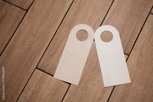 Two blank door hanger mockups in white on a wooden surface. Ideal for hotel branding, “Do Not Disturb” or cleaning service signage design templates.