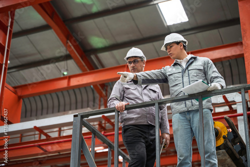 Engineers inspecting equipment and discussing maintenance procedures inside a modern industrial factory. Safety, teamwork, and production quality control in a manufacturing plant.