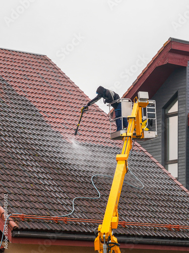 Professional worker cleaning roof tiles with high-pressure washer from yellow lift platform