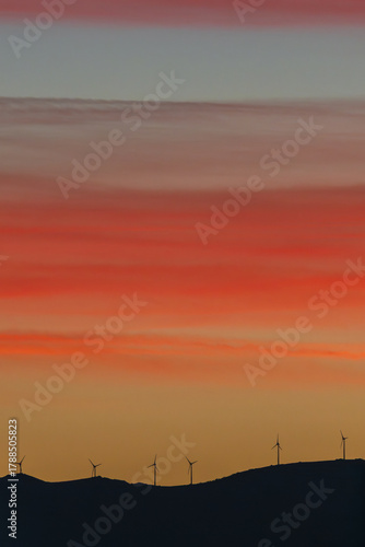 A red-hot sky above a mountain range dotted with wind turbines