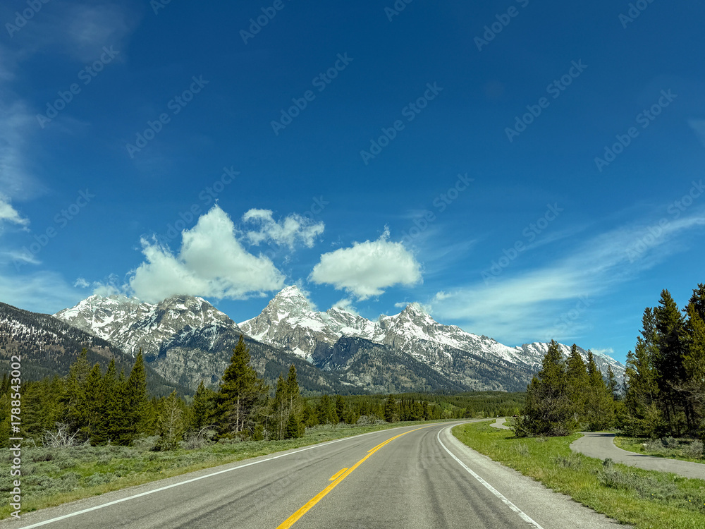 Fototapeta premium Scenic landscape view of a snow capped mountains from a car driving on a road through the Grand Teton national Park. No people.