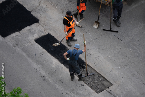 Road construction workers repairing damaged asphalt pavement with shovels and rakes, focused on restoring urban infrastructure and safety