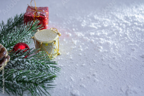 Festive Christmas and New Year scene with a golden drum, a red gift box with a bow, and a pine cone on pine branches. The festive composition includes space for a greeting card.