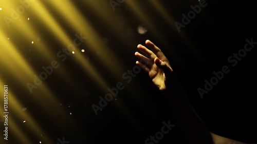 A human hand reaches out toward the shimmering divine rays of bright golden light in the darkness. Magic dust slowly floats in the rays of light. 4K concept slow motion video 60 fps.