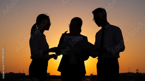 Silhouette of successful business team discussing project against a vibrant sunset backdrop