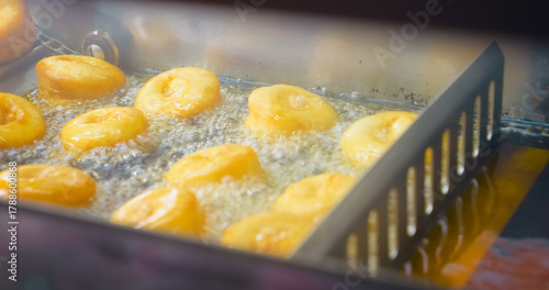 Automated donut production line featuring golden pastries deep frying in bubbling hot oil at industrial bakery manufacturing facility