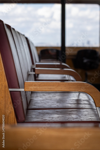 Empty ferry boat chairs with wooden armrests and worn leather seats and window, Istanbul, Türkiye