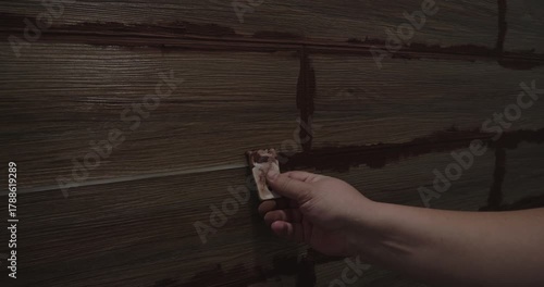 Tiler applying brown grout to the joints between wood-look ceramic tiles on a wall, using a small rubber spatula to fill the gaps during a home renovation project and finishing process.