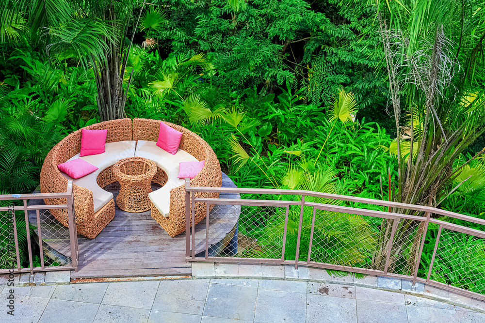 Obraz premium A circular rattan seating area with pink cushions against a backdrop of lush tropical plants in Yanoda Park, Sanya, Hainan, China