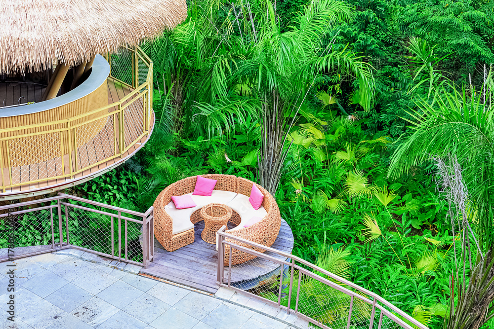 Naklejka premium A circular rattan seating area with pink cushions against a backdrop of lush tropical plants in Yanoda Park, Sanya, Hainan, China