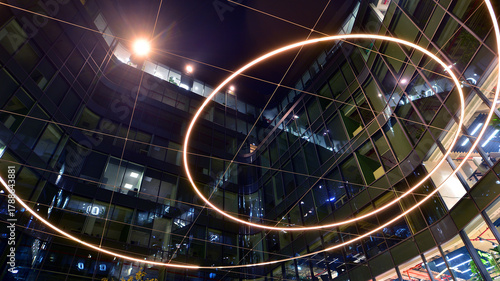 Modern office building in city center illuminated at night. Green trees near a modern office building with a glass facade. Rows of lit windows against the architectural grid of a modern facade.