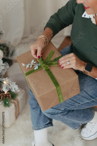 Midlife woman hands wrapping holiday present with green ribbon