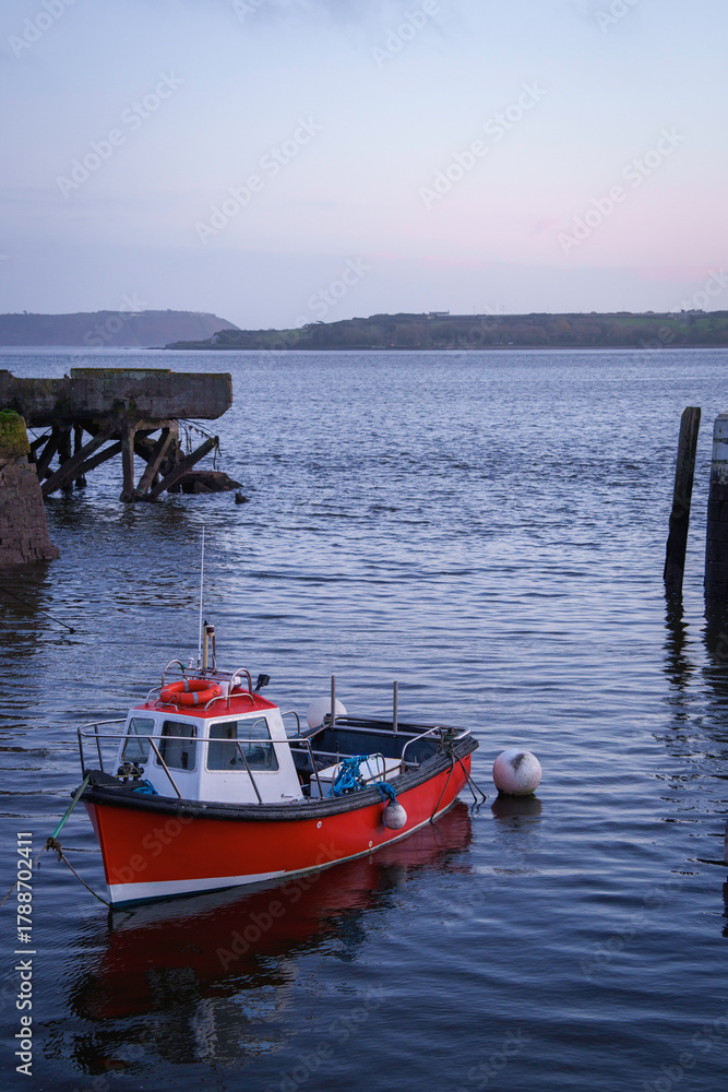 Fototapeta premium A red fishing boat moored at low tide in Cobh harbor, County Cork, Ireland.