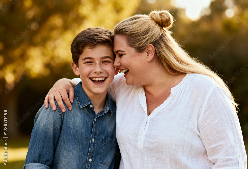 Fototapeta premium A happy mother and her son laughing and embracing outdoors. Joyful family enjoying quality time together in a park during golden hour.