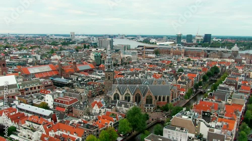 Drone shot over Amsterdam city center with Oude Kerk, traditional Dutch architecture, red roofs, and canal layout. Perfect for travel, tourism, and urban heritage content. 4K establishing aerial view