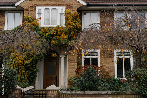 Row of traditional English brick houses partially covered with colorful autumn climbing plants. Quiet residential architecture in a leafy London neighborhood.