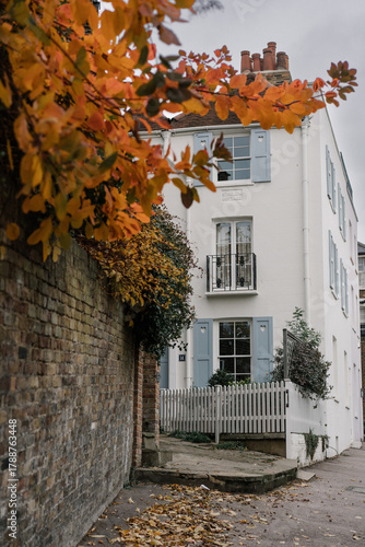 Charming white period house at the end of a narrow lane framed by an old brick wall and vivid orange autumn foliage in Hampstead, London, UK.
