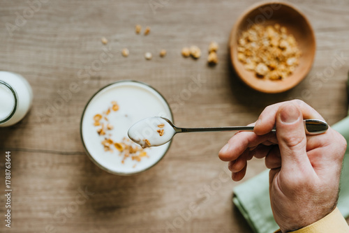 Top view of man adding granola to yogurt bowl on wooden background