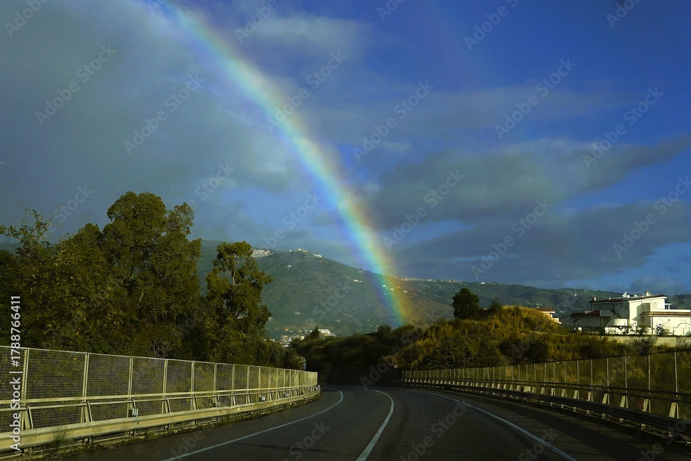 Obraz premium A rainbow through a wet car windshield. Road trips. An atmospheric and dynamic landscape capturing the contrast between rain and sun.