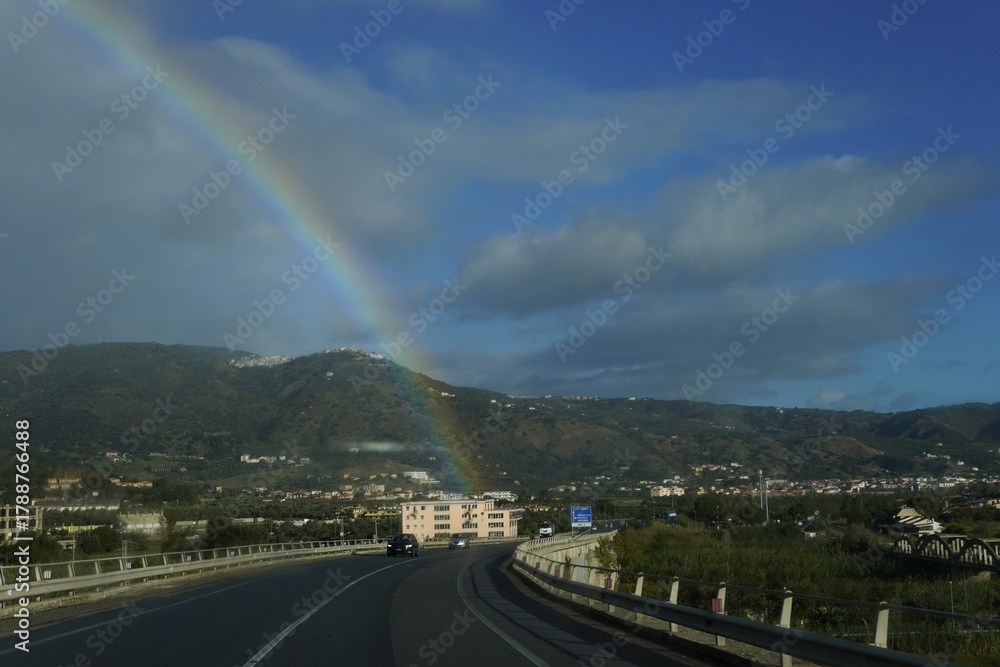 Obraz premium A rainbow through a wet car windshield. Road trips. An atmospheric and dynamic landscape capturing the contrast between rain and sun.