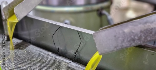 Close-up of fresh extra virgin olive oil flowing from stainless steel pipes during extraction at an olive mill
