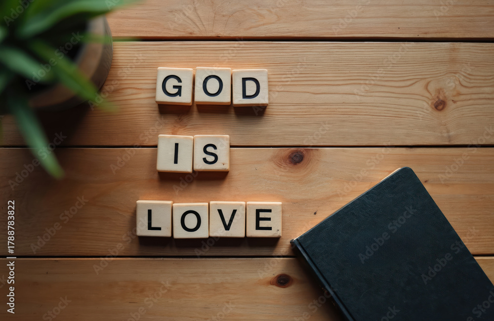 Naklejka premium Wooden table with letter tiles spelling God is Love, a closed book and a plant. Top view flat lay with copy space for text. Religious concept for faith and belief.