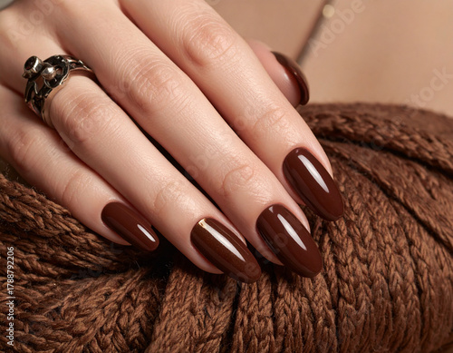 Beautiful brown manicure on a woman's hand. Manicure with burgundy semi-permanent nail polish applied to oval nails
