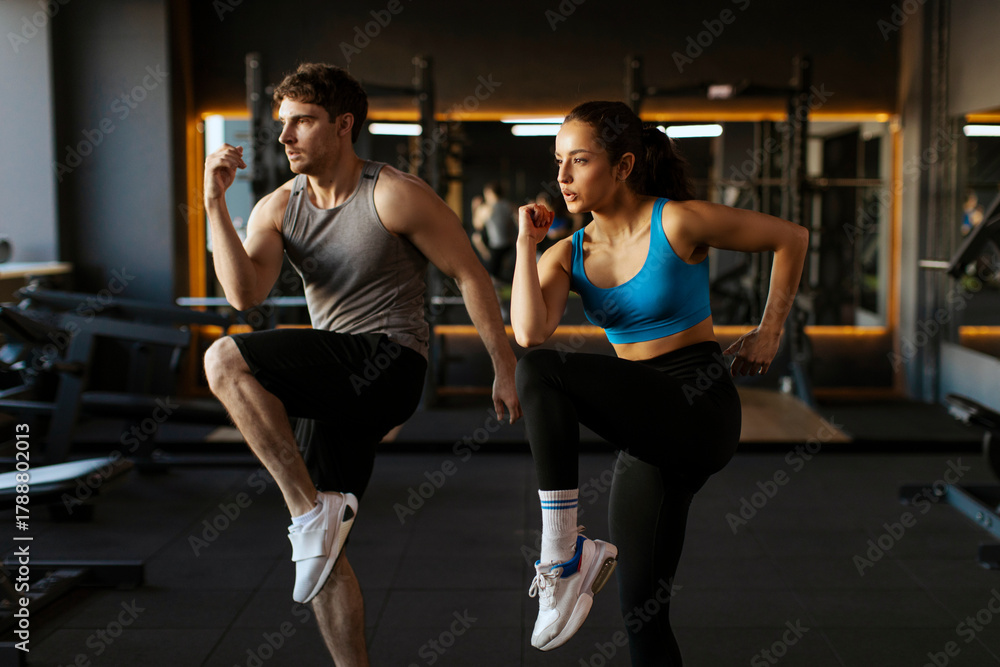 Fototapeta premium Man and woman performing high-intensity interval training exercise in well-equipped gym, demonstrating effort and determination in fitness routine