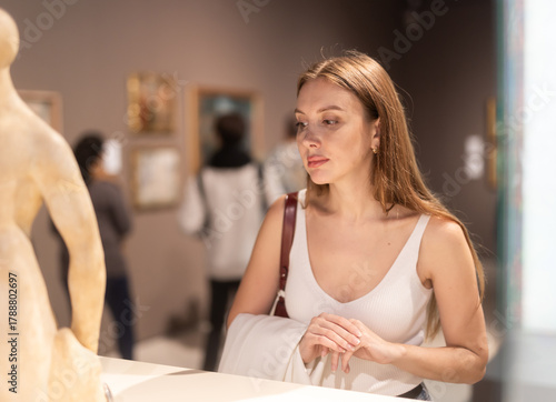 Girl walk along exhibition pavilion, get acquainted with statuary. Statues made of marble, metal, ceramics with detailed description and explanatory note