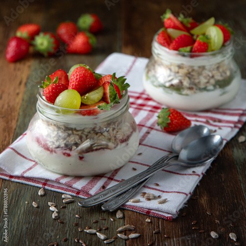 Homemade yogurt with muesli, strawberries and grapes in glass jars on a wooden table