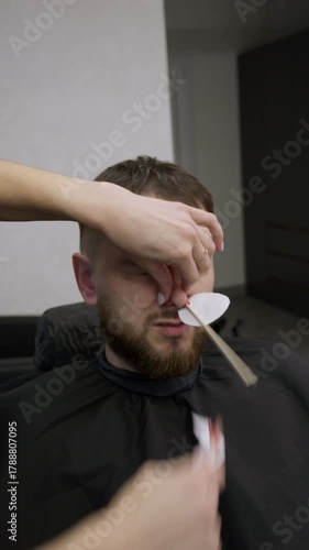 Barber removing hair in nose by waxing from Bearded Man face in stylish barbershop. Beautician hair removal procedure in male beauty salon. Male skin care and beard style concept